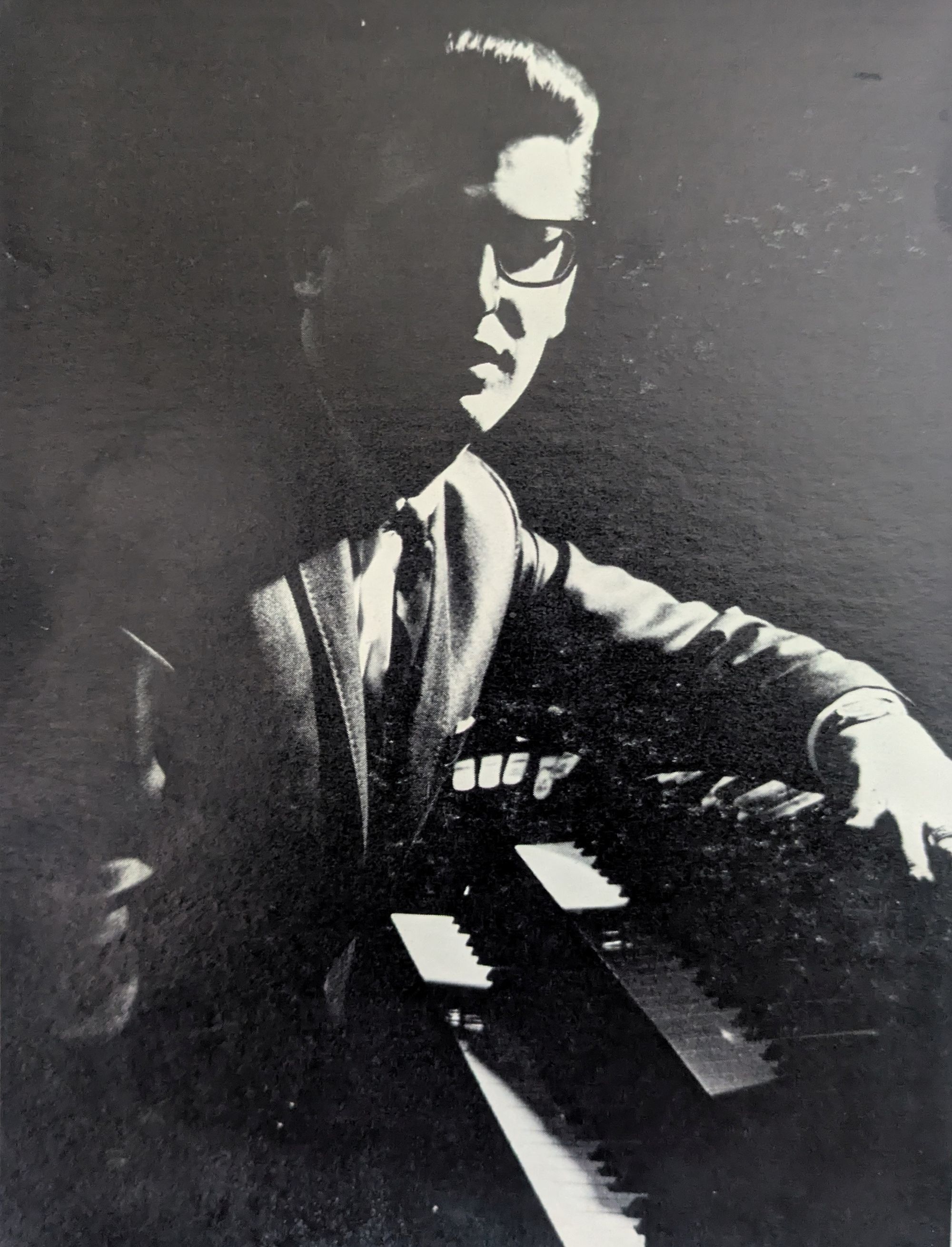 A picture of Skip at the organ, wearing glasses, his face half-obscured by the stark lighting